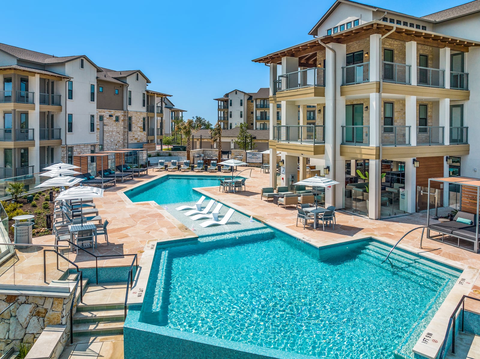 The Artesian at Bee Cave resort pool with in-water loungers and cabanas below the pool building, from above